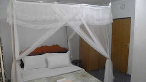A bed with a canopy, a wooden headboard, and a rolled towel on the bed. - Imani Radio & TV Ministries (Kitale)