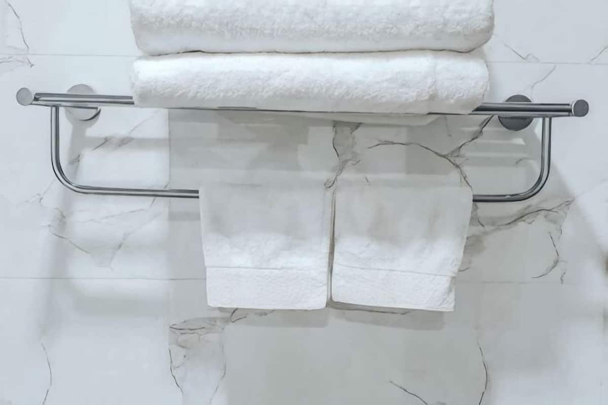 A bathroom with a marble wall, a towel rack with folded towels, and a metal grab bar.