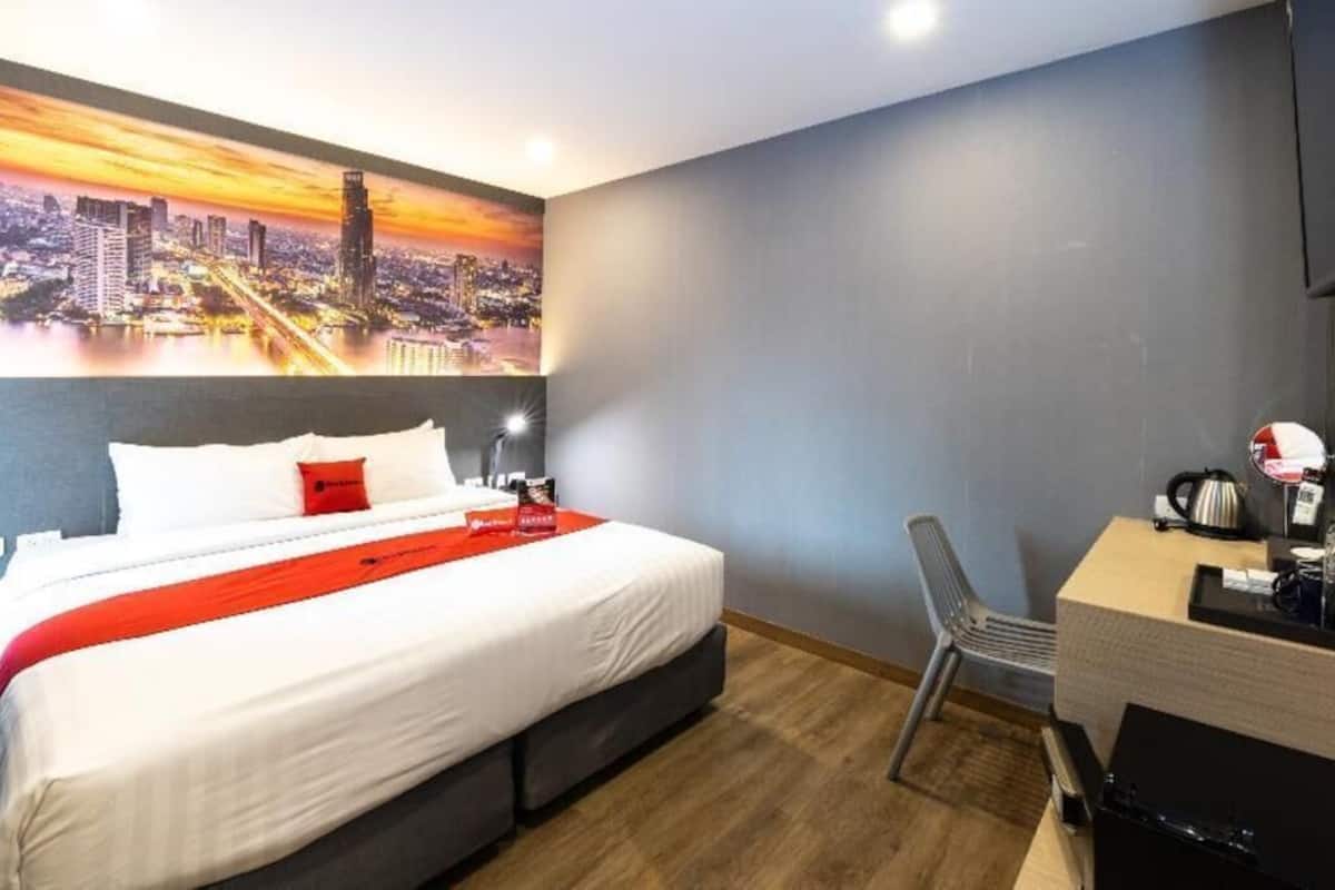 A hotel room with a bed, a desk, a chair, and a cityscape mural on the wall.
