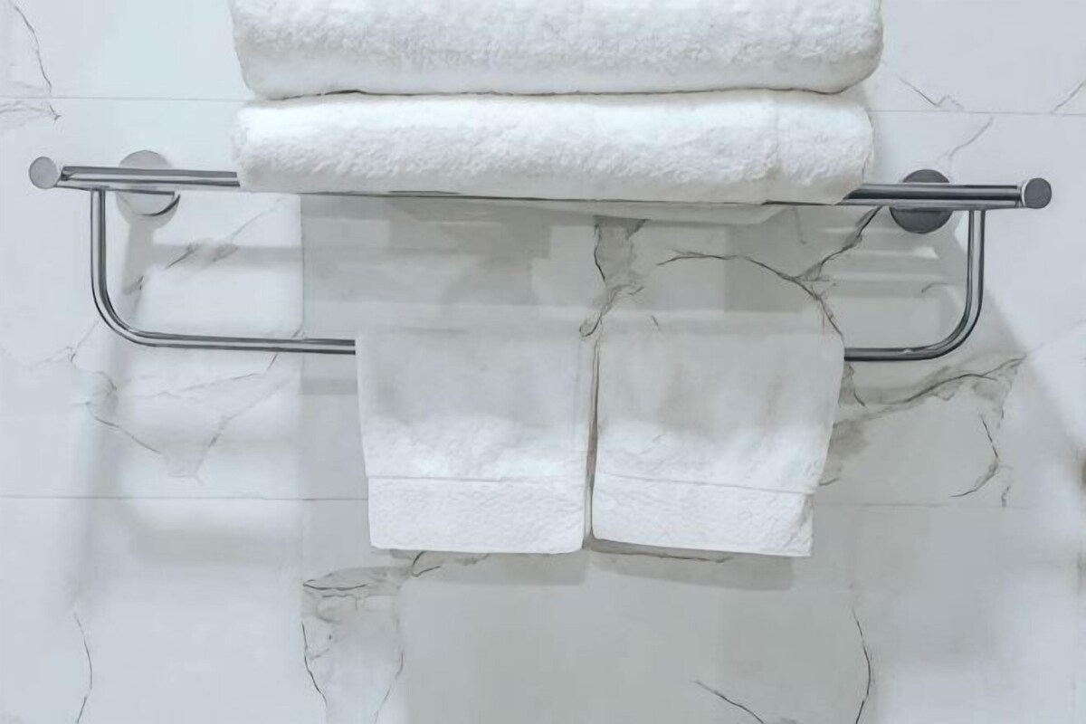 Un baño con pared de mármol, un perchero con toallas dobladas y una barra de apoyo metálica.
