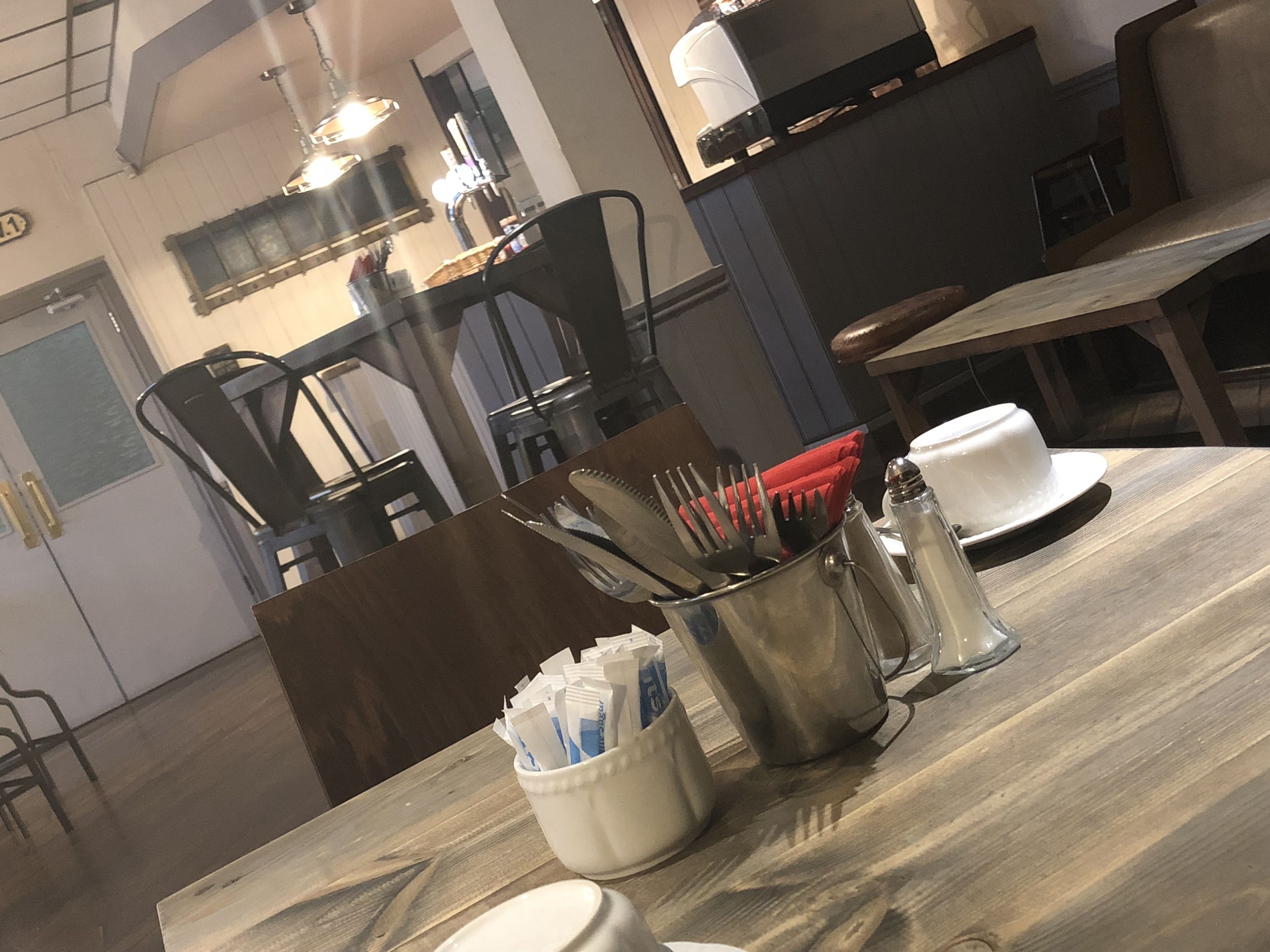 A dining area with a wooden table, metal utensil holder, salt and pepper shakers, and a white cup.