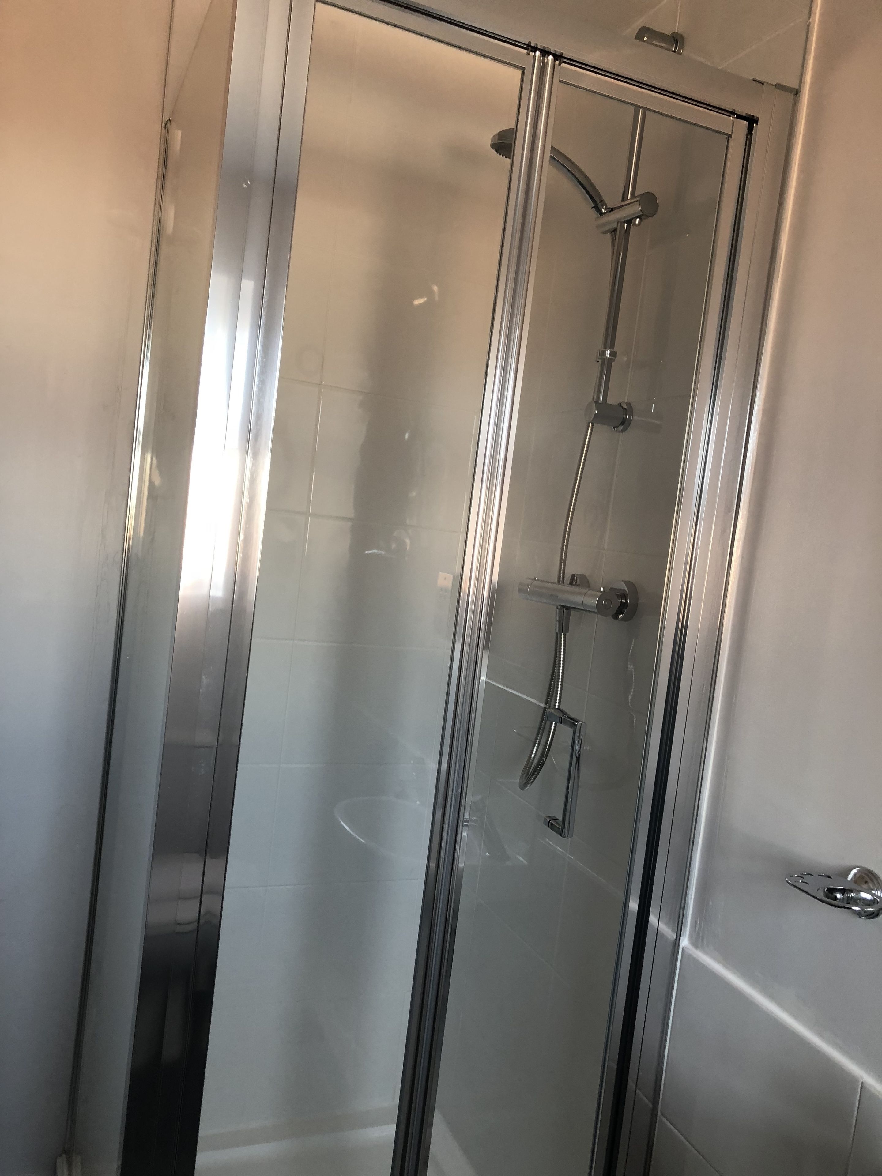 A glass-enclosed shower stall with a handheld showerhead and a wall-mounted faucet.