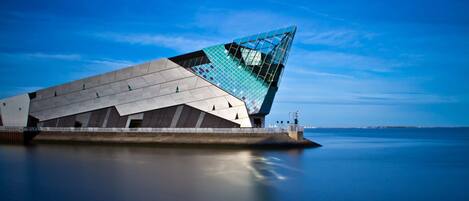 Un edificio moderno de arquitectura con un diseño angular distintivo, ubicado junto a una masa de agua tranquila.