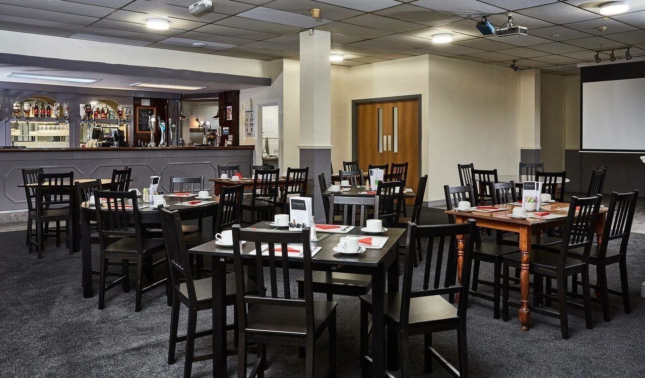 Una sala de conferències amb diverses taules i cadires, una zona de bar i una pantalla de projecció.