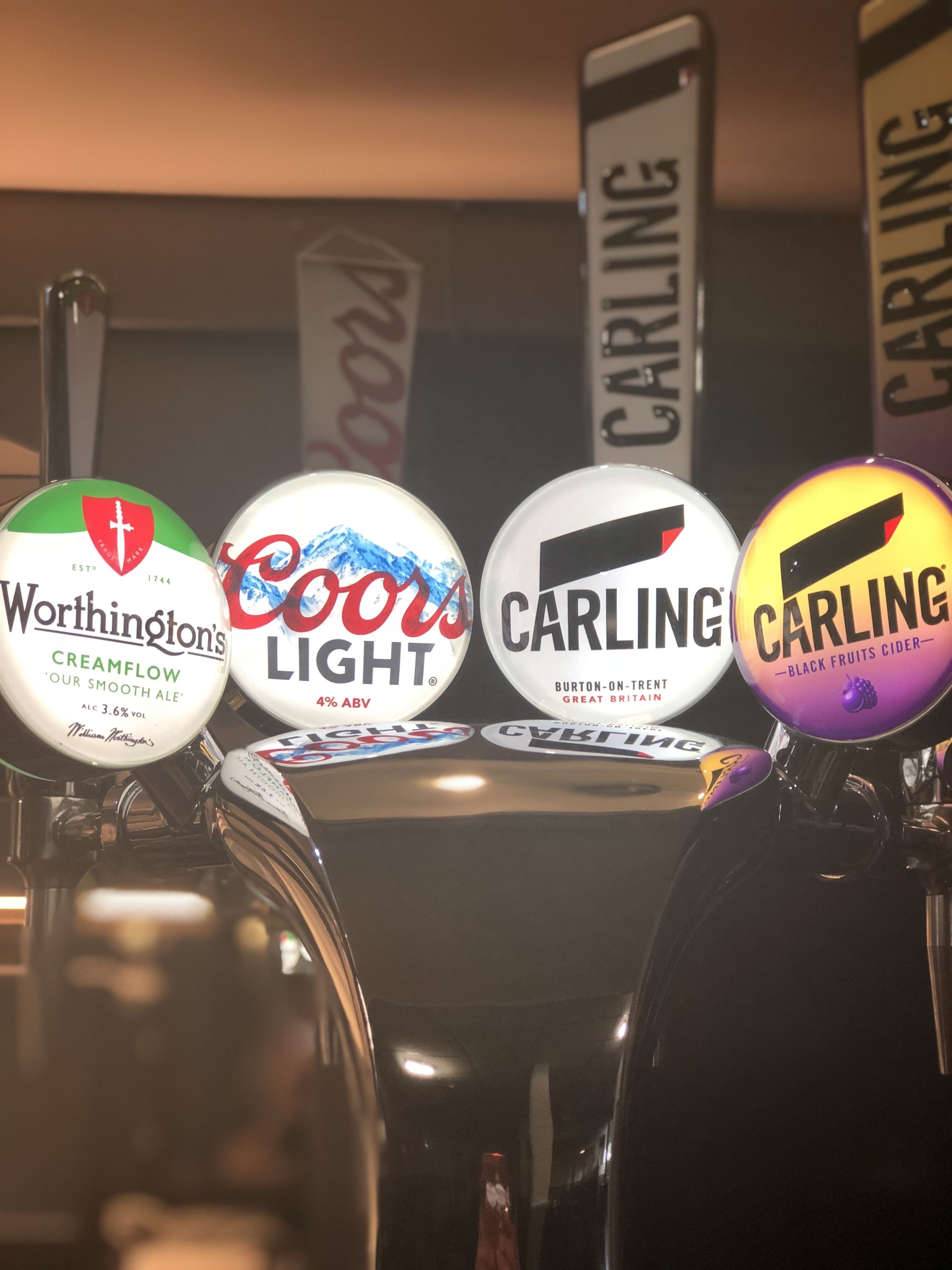 Una hilera de grifos de cerveza con etiquetas para las cervezas Worthington's Creamflow, Coors Light y Carling.