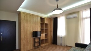 Uma sala de estar com um armário de madeira, uma televisão de tela plana, um sofá e um aparelho de ar condicionado.