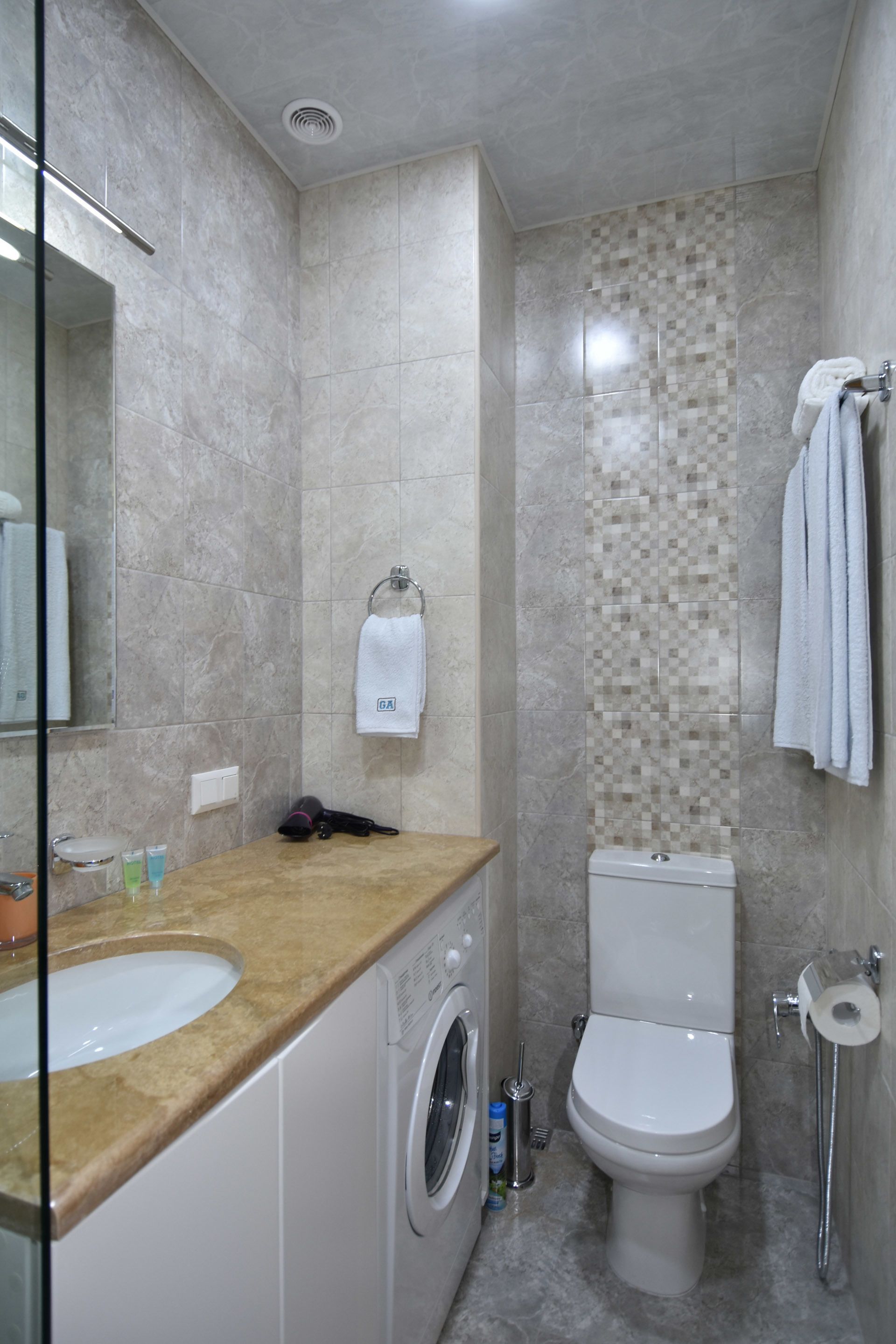 A bathroom with a sink, washing machine, toilet, and shower.