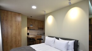 Quarto de hotel compacto com cama, cozinha compacta e pequena área de refeições.