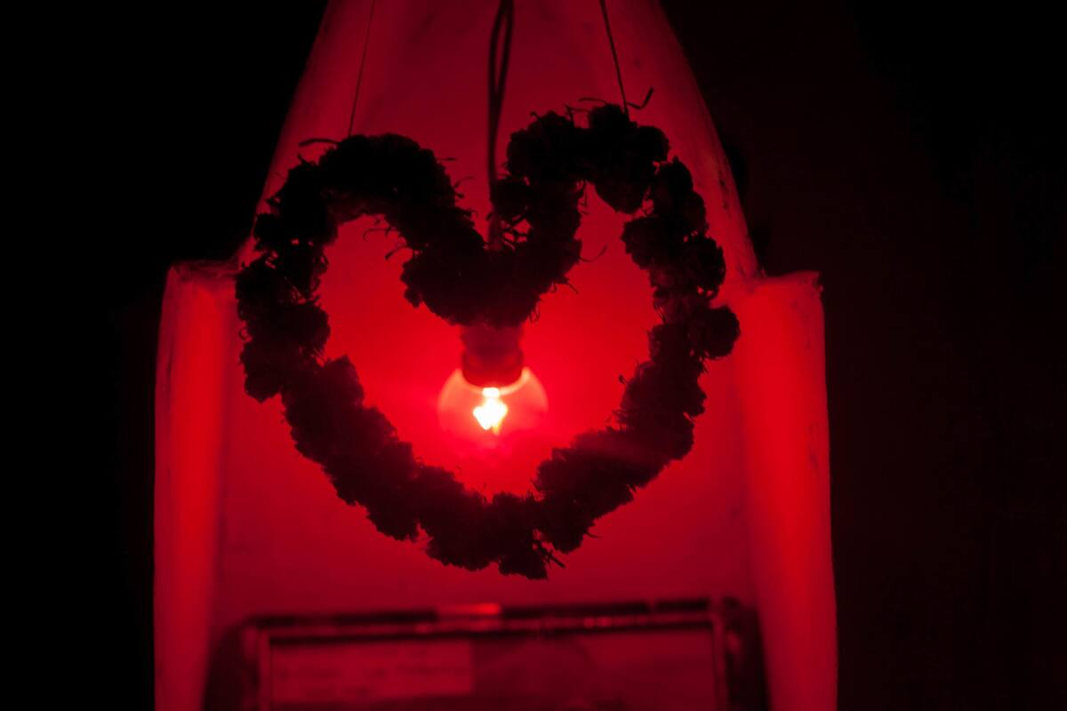 A heart-shaped light fixture with a red glow, a framed picture below, and a small white object on a table.
