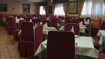 Un salón de banquetes con filas de mesas y sillas, cada conjunto con manteles blancos y sillas rojas.