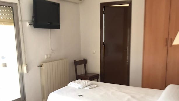 A hotel room with two beds, a television mounted on the wall, a radiator, a wooden door, and a window with blinds. - Hotel Mesón del Moro (Abaran)