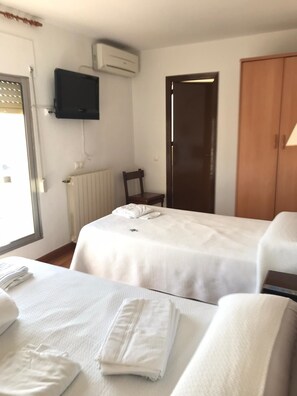 Ein Hotelzimmer mit zwei Betten, einem an der Wand befestigten Fernseher, einem Heizkörper, einer Holztür und einem Fenster mit Jalousien.