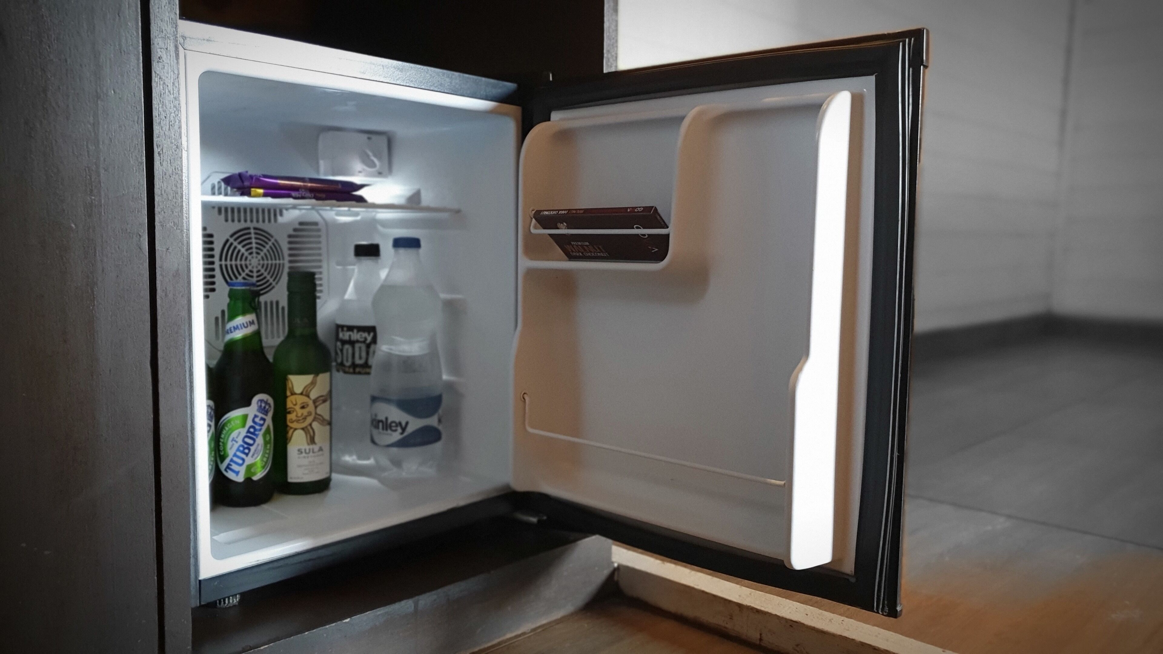 Un réfrigérateur ouvert, avec des étagères contenant des bouteilles de boissons et un livre.
