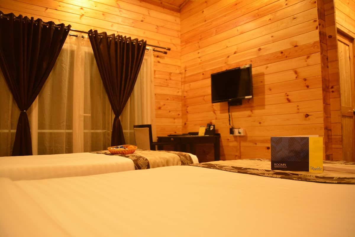 A wooden cabin room with two beds, a television, and a box labeled "ROOMIN."