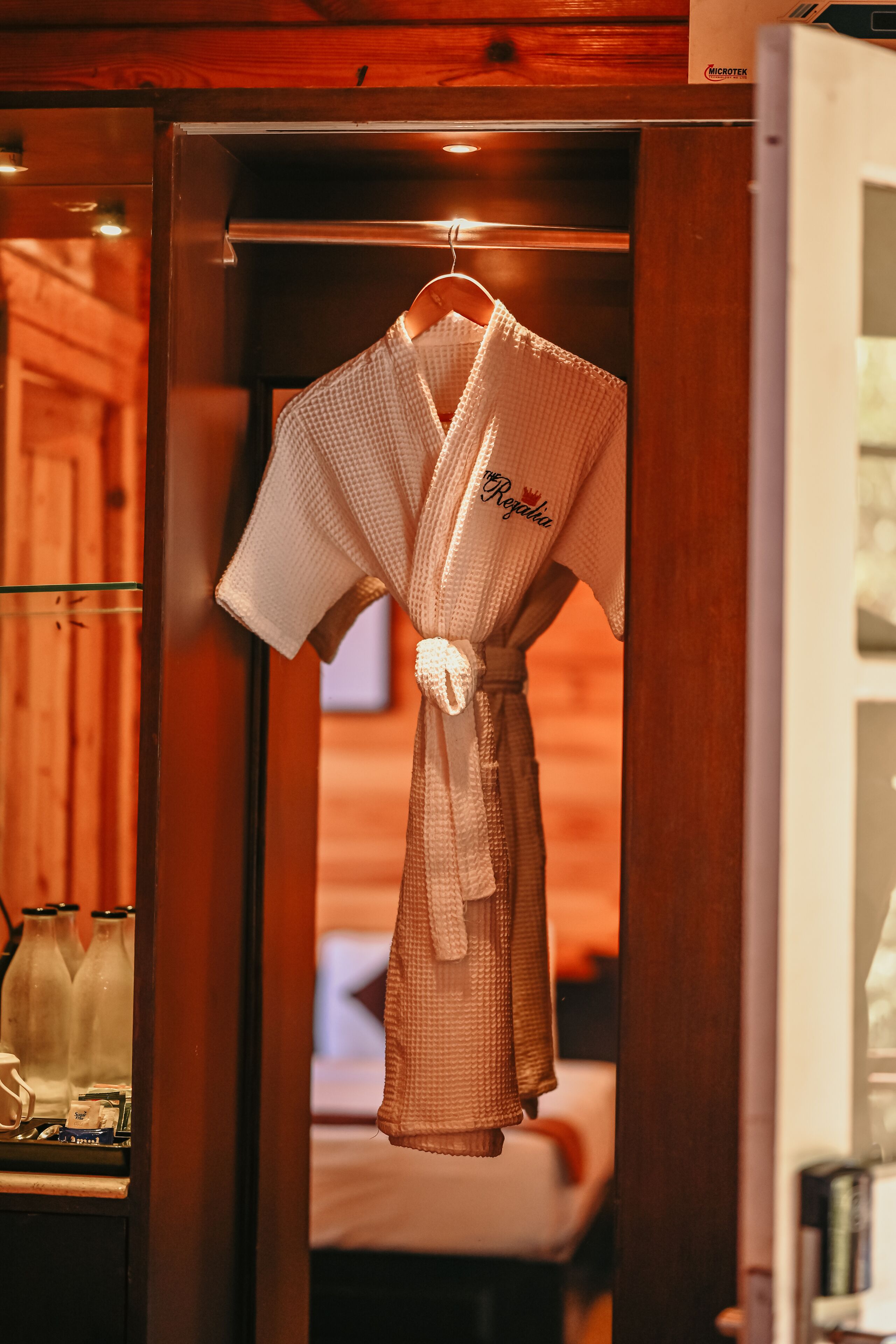 A robe hanging in a wooden room with a bed and a shelf with bottles.