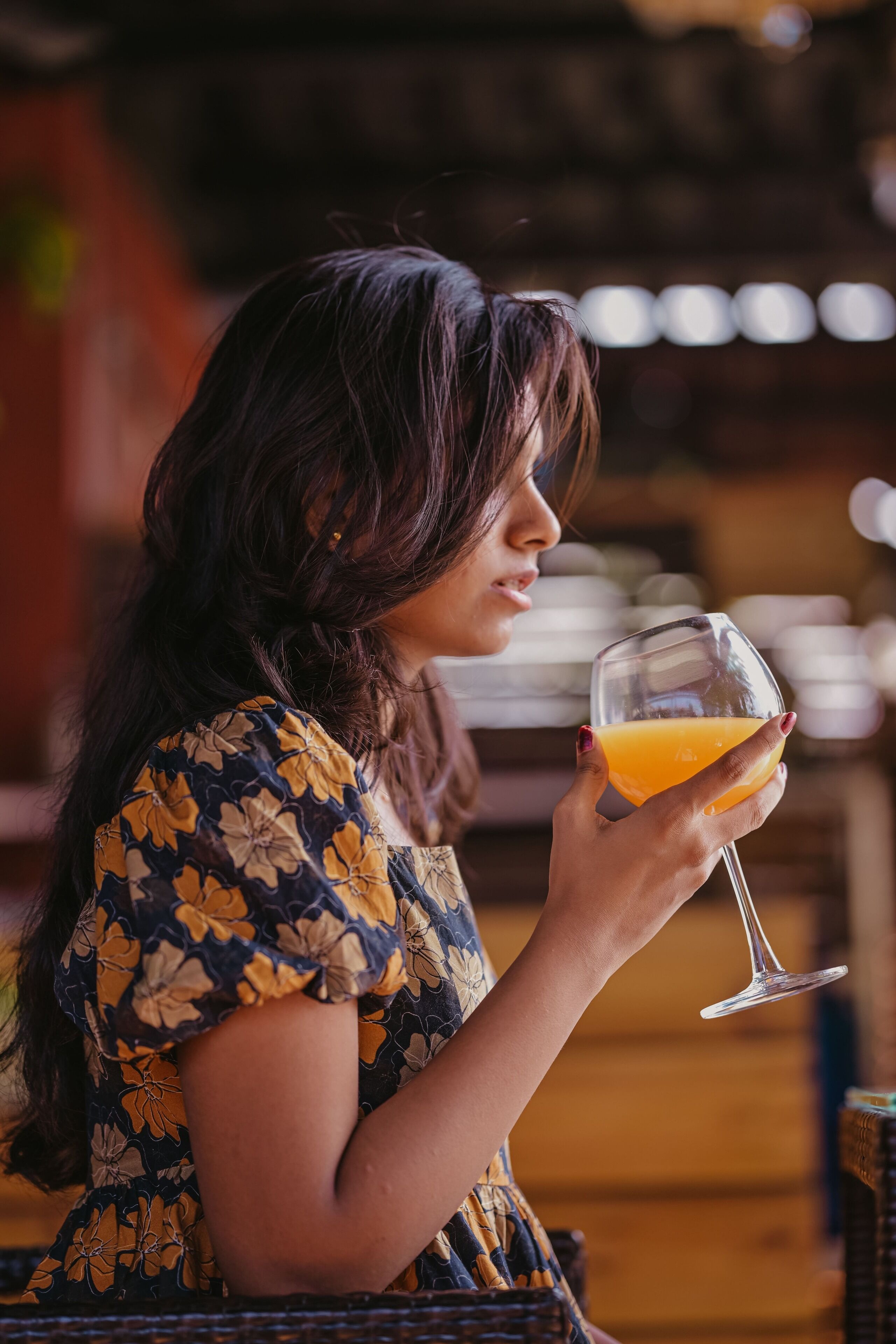 A person holding a glass of orange juice in a casual setting with wicker furniture.