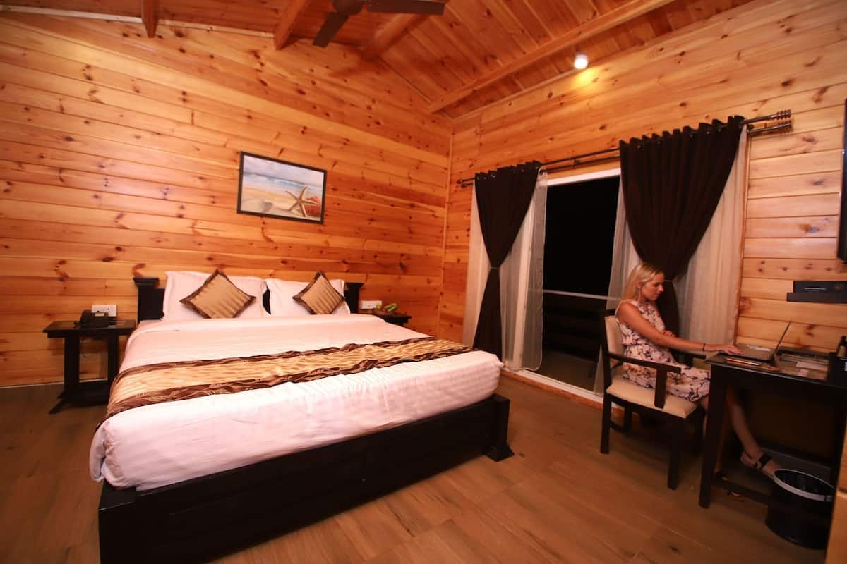 A wooden cabin room with a bed, a desk, and a window with curtains.
