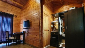 A wooden cabin interior with a dining area, a kitchen with a refrigerator, and a television mounted on the wall. - The Regalia Resort (Ashvem)