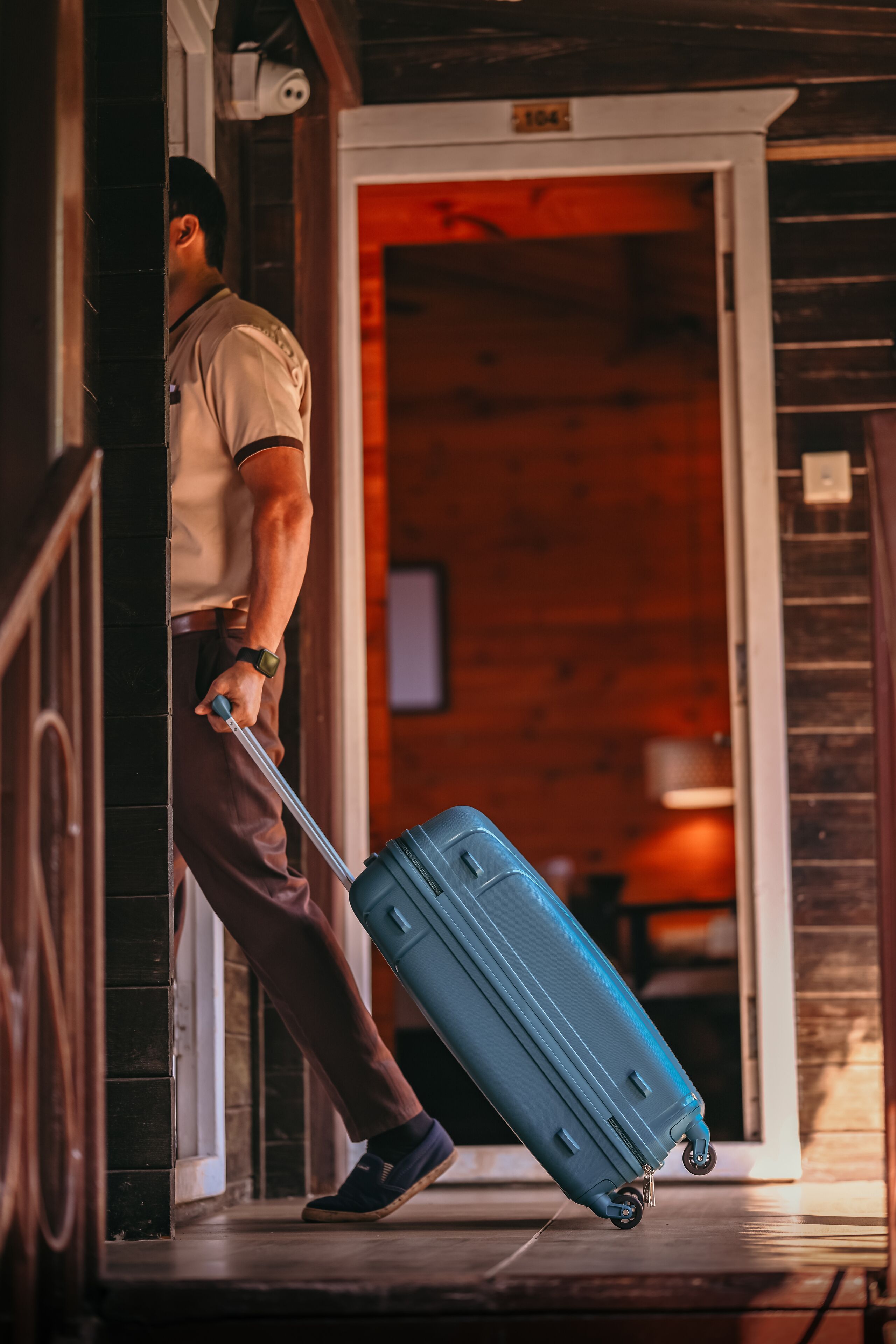 A person carrying a blue suitcase through a wooden door into a room with a visible television.