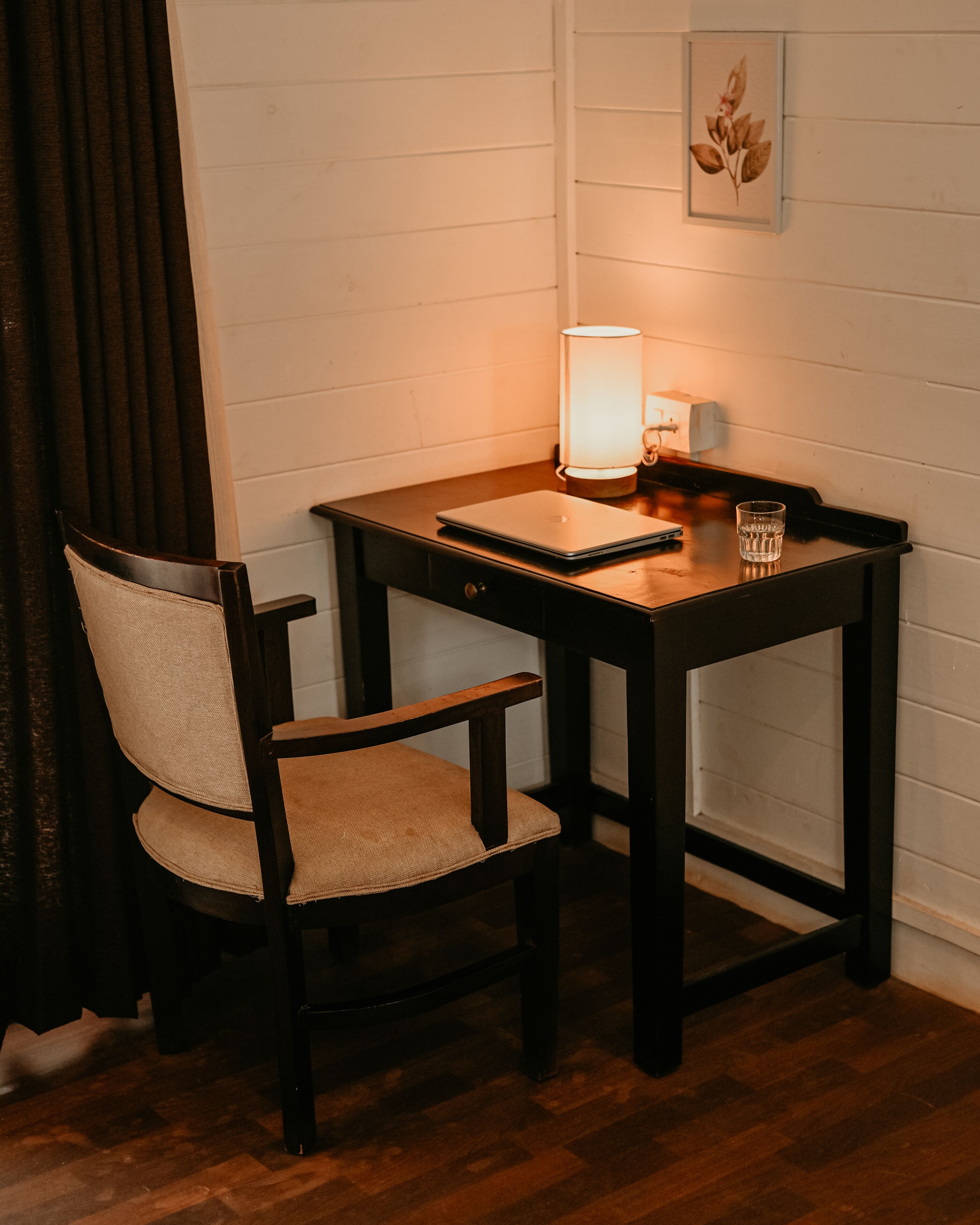 A small wooden desk with a laptop, a lamp, and a glass of water.