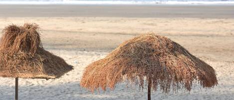 A beach with two straw umbrellas and white lounge chairs.