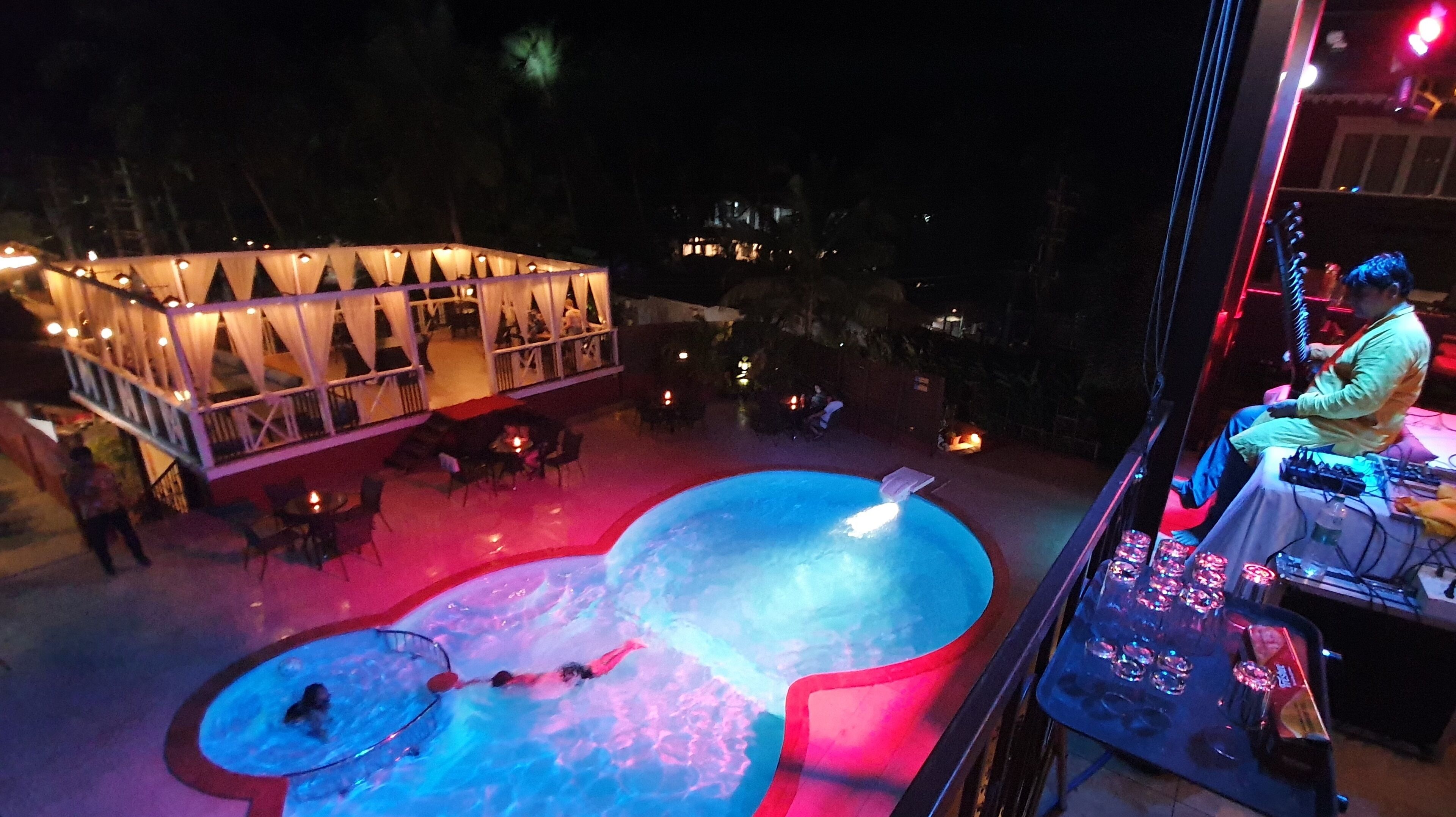 Ein Poolbereich mit Wasserrutsche, umgeben von Tischen und Stühlen, und ein Gebäude mit Dreiecksfenstern im Hintergrund.