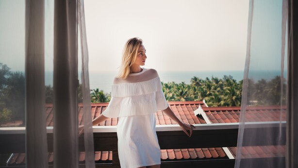 A person standing on a balcony with a view of the ocean and palm trees. - The Regalia Resort (Ashvem)