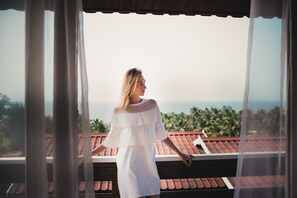 Iemand staat op een balkon met uitzicht op de oceaan en palmbomen.