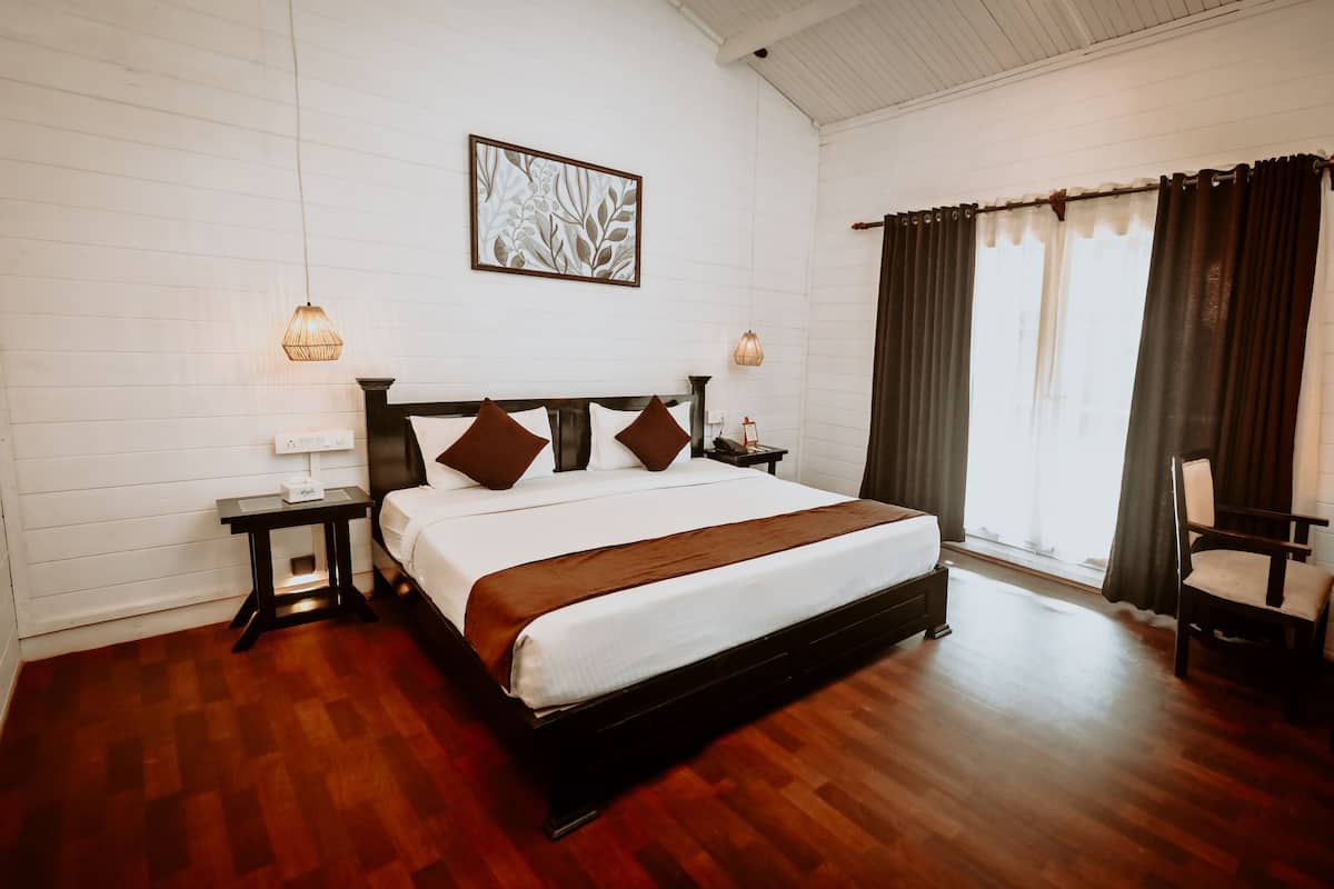 A neatly arranged bedroom with a large bed, bedside tables, a wall-mounted artwork, and a window with curtains.