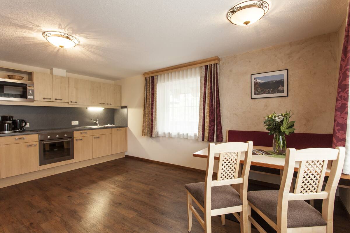A modern kitchen with wooden cabinets, a dining table with chairs, and a window with curtains.