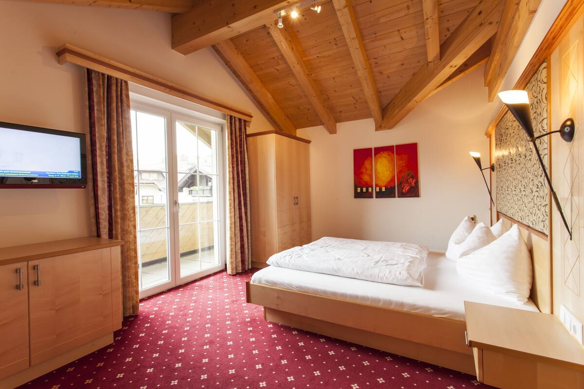 A bedroom with a wooden ceiling, a bed, a TV, and a sliding glass door.