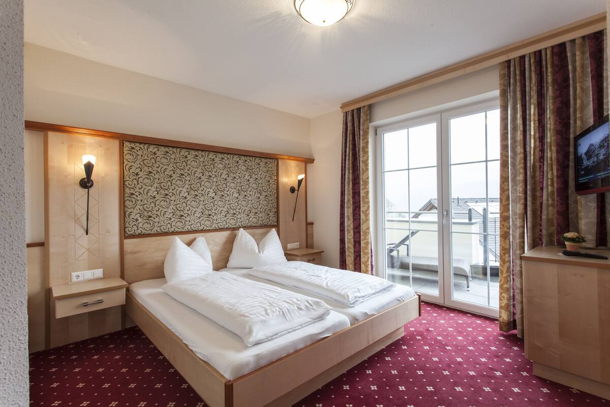 A hotel room with a large bed, two bedside tables, a TV, and a view of the outside.