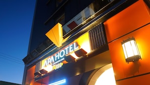 The exterior of the APA Hotel with a prominent sign and illuminated entrance.