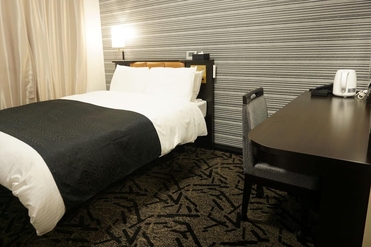 A hotel room with a bed, a desk, a chair, and a patterned carpet.