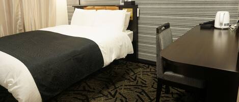 A hotel room with a bed, a desk, a chair, and a patterned carpet.