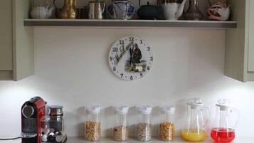 A kitchen with a clock, a coffee maker, and containers of spices.
