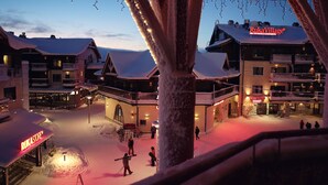 Ein verschneiter Innenhof mit Gebäuden, darunter ein Hotel und ein Geschäft, und Personen, die sich darin aufhalten.
