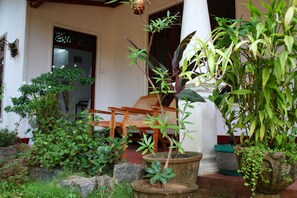 A traditional house with a wooden chair outside, surrounded by various potted plants.