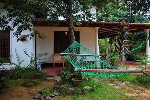 A hammock tied between trees in a garden area with a white building in the background.