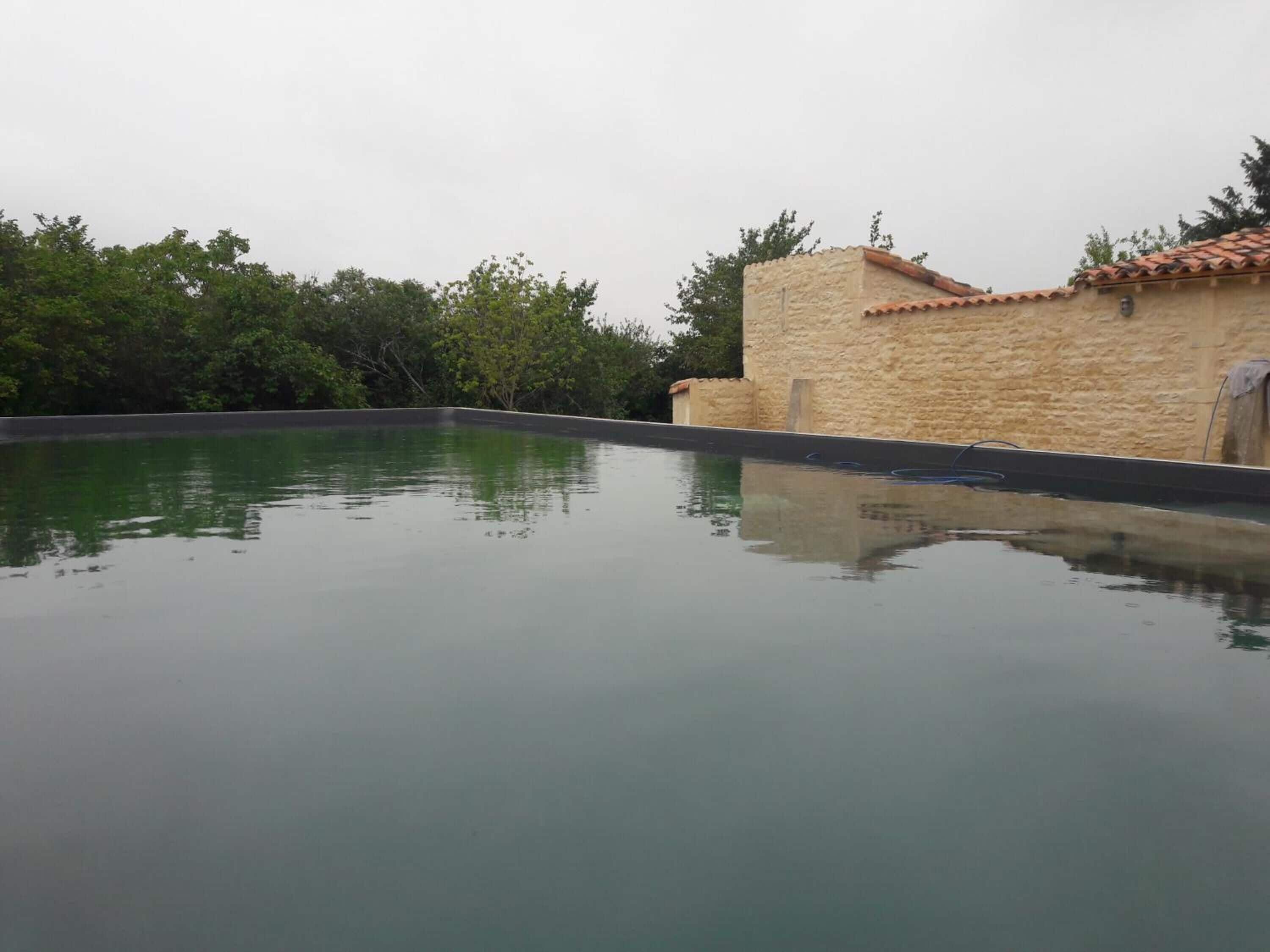 A swimming pool with a stone wall and tiled roof in the background.