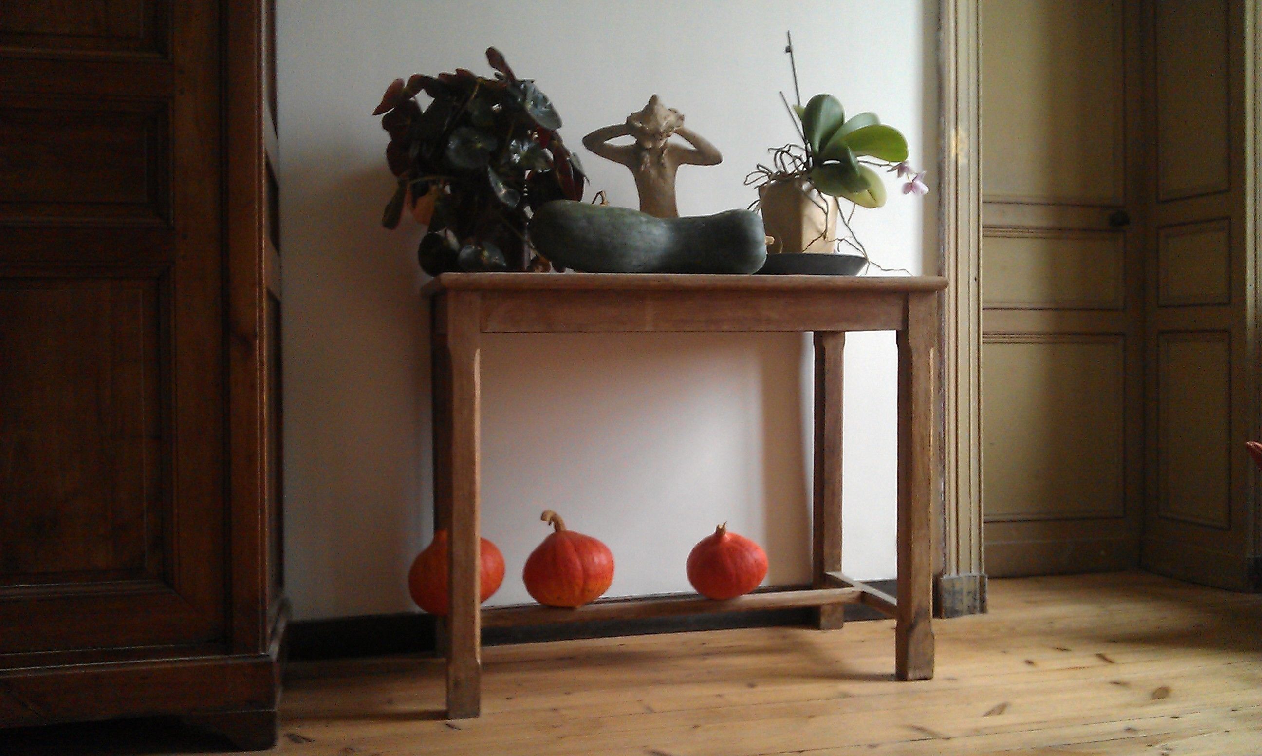 Een houten tafel met een bloempot, een klein beeldje en twee pompoenen op een houten vloer.