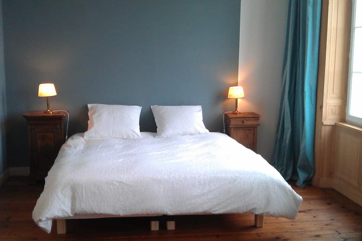 A bed with white linens, two bedside tables with lamps, and a window with curtains.