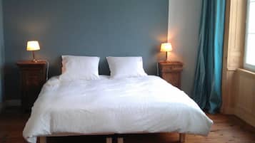 A bed with white bedding, two bedside tables with lamps, a wooden floor, and a window with blue curtains.
