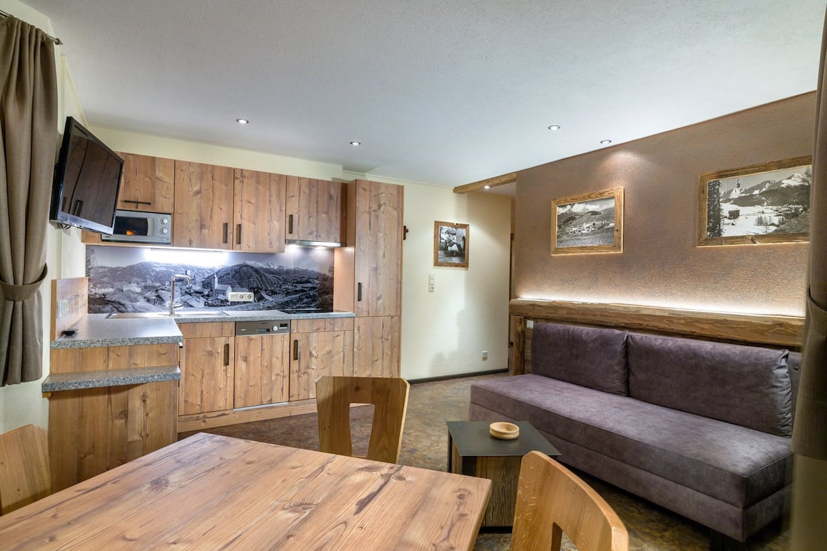 A compact kitchen with wooden cabinets, a built-in microwave, and a large window displaying a mountainous landscape.