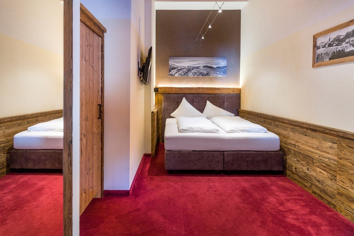 A hotel room with a bed, a wooden door, a red carpet, and a painting on the wall.