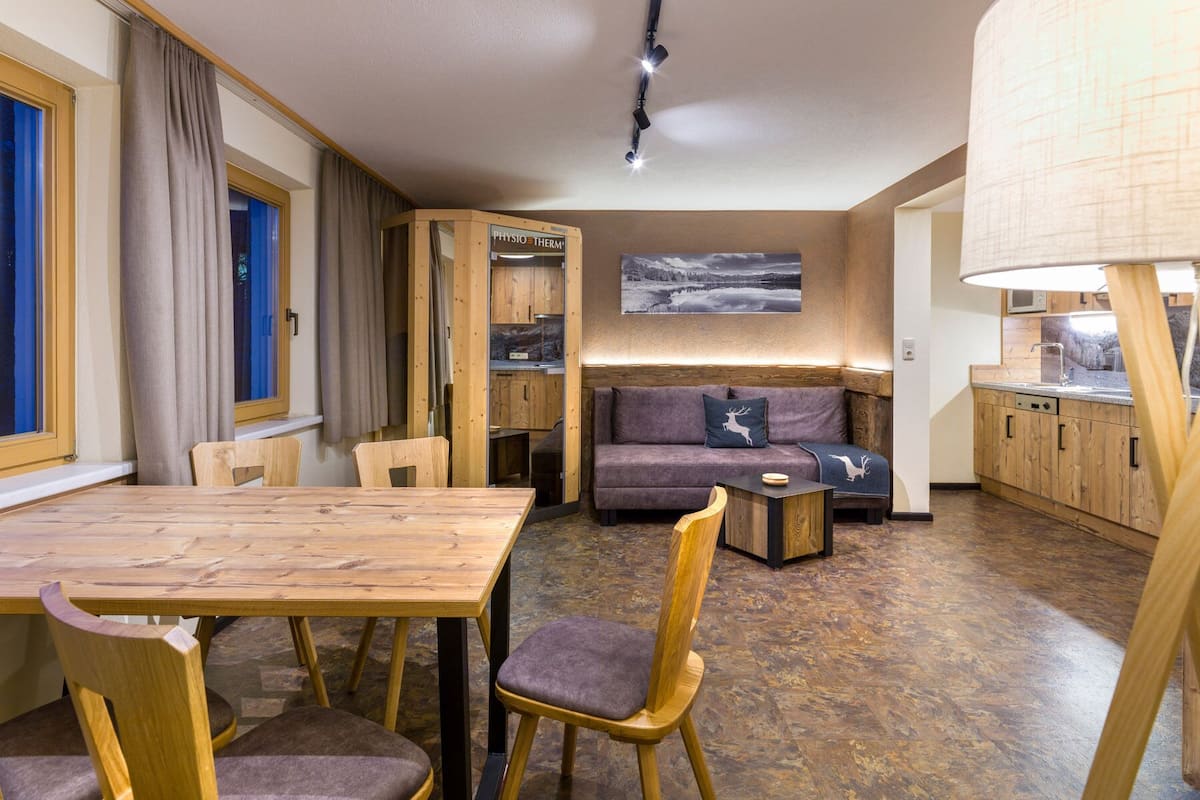 A compact living space with a wooden dining table, a sofa, and a kitchenette.