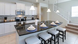 A modern kitchen with white cabinets, a central island with bar stools, a microwave, and a stove. - Fv66383 - Windsor At Westside - 5 Bed 4.5 Baths Townhome (Kissimmee)