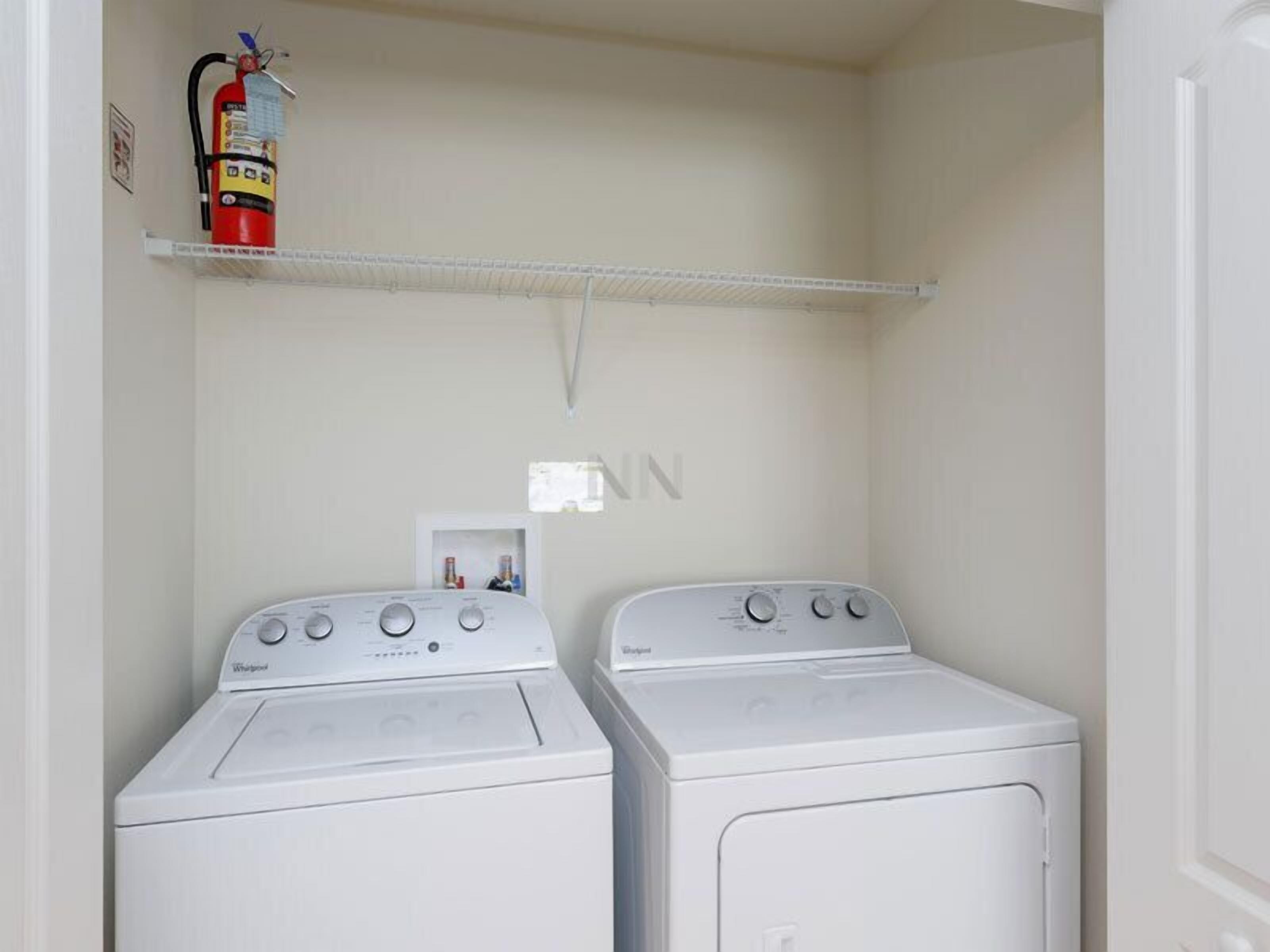 A laundry room with two Whirlpool washers and a fire extinguisher on a shelf.