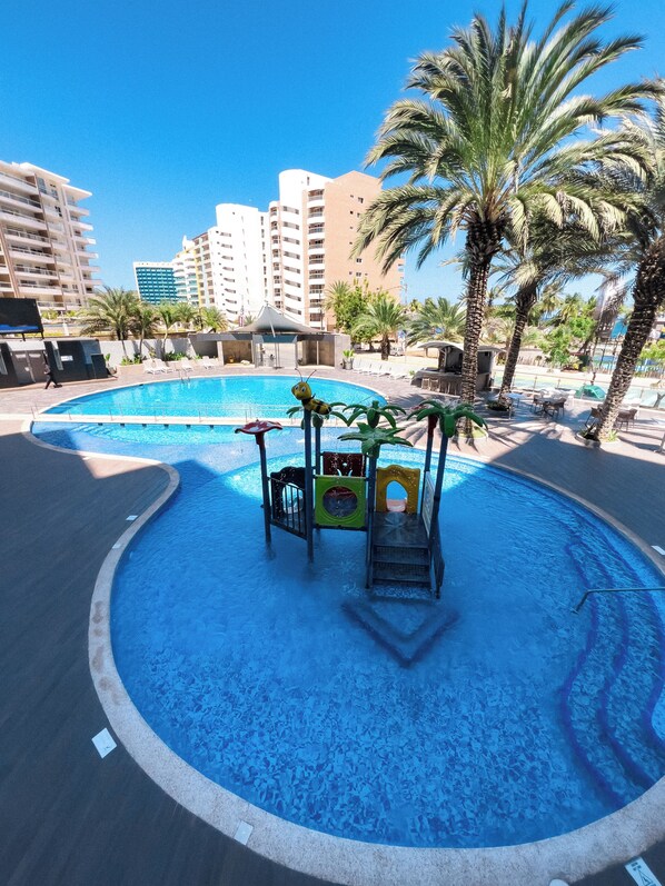 A children's play area with a pool, palm trees, and a view of high-rise buildings. - Tibisay Hotel Boutique Margarita (Maneiro)