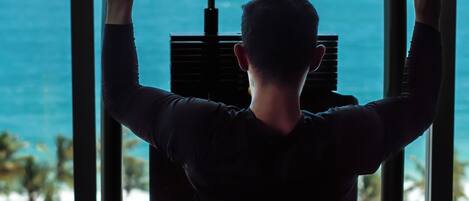A person exercising on a pull-up bar with a view of the ocean through large windows.